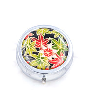 Silver metal pill box featuring green, red, and white maples leaves on a black background with metallic gold accents.