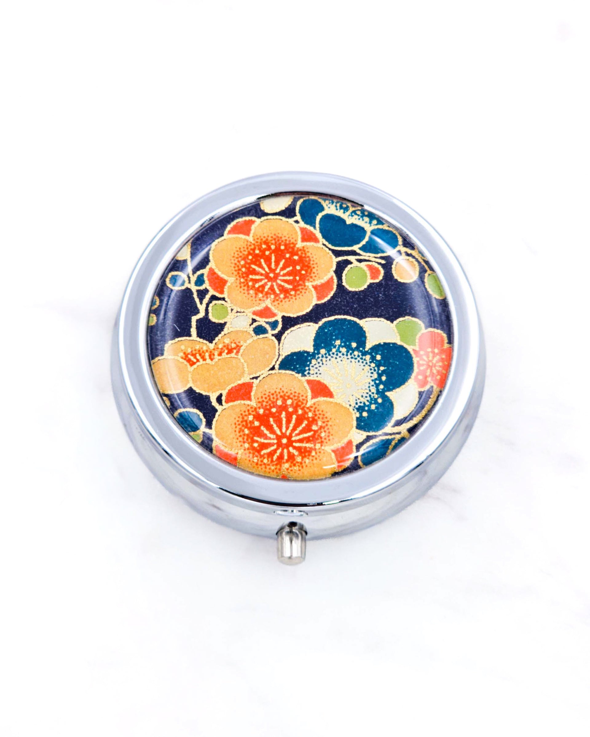 Silver metal pill box featuring orange and blue plum blossoms on a dark blue background with metallic gold accents.