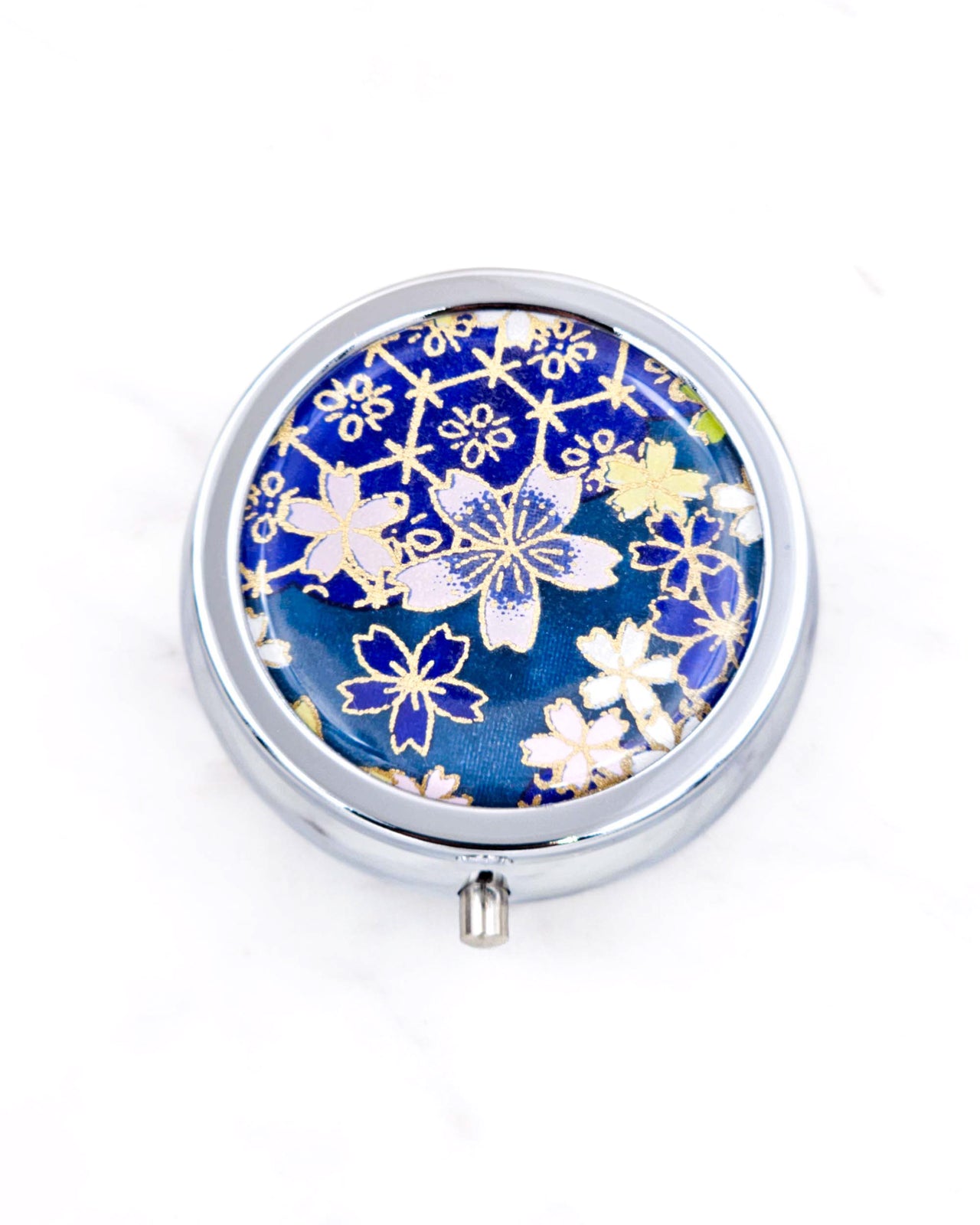 Silver metal pill box featuring pink and blue cherry blossoms on a dark blue background with metallic gold accents.