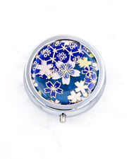 Silver metal pill box featuring pink and blue cherry blossoms on a dark blue background with metallic gold accents.