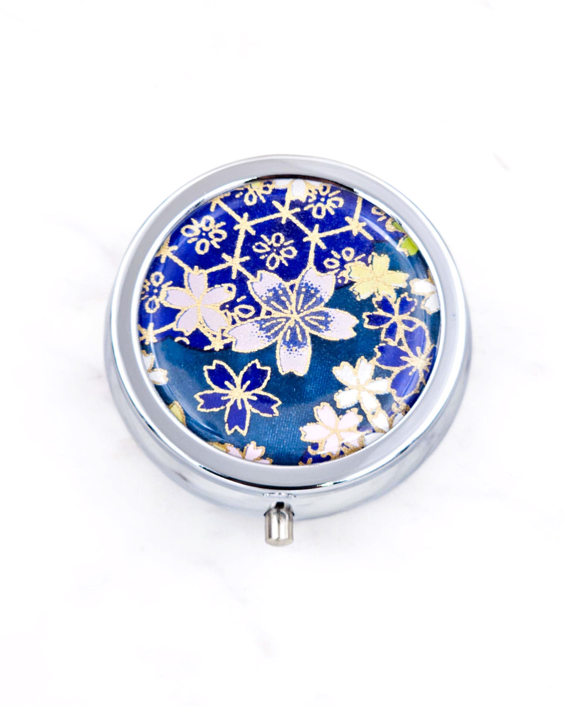 Silver metal pill box featuring pink and blue cherry blossoms on a dark blue background with metallic gold accents.