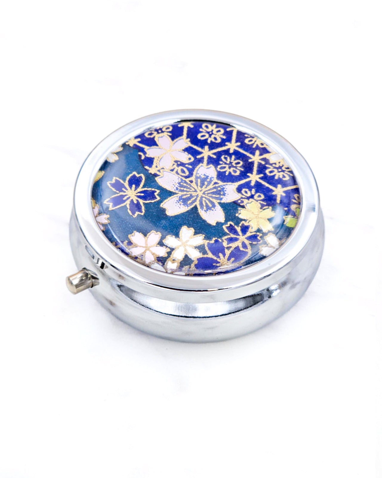 Silver metal pill box featuring pink and blue cherry blossoms on a dark blue background with metallic gold accents.
