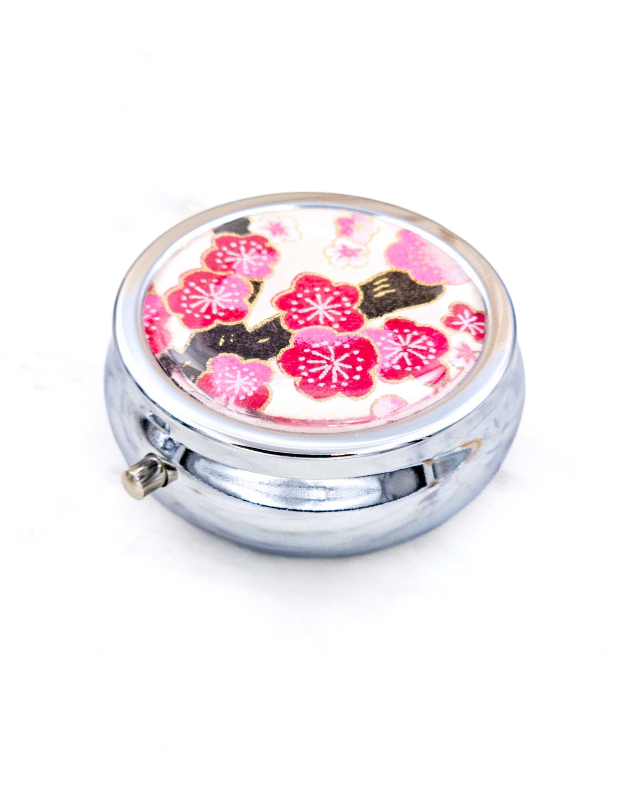 Silver metal pill box featuring a pink plum blossom tree on a white background with metallic gold accents.