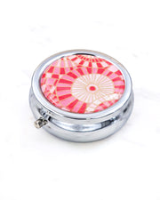 Silver metal pill box featuring pink and white abstract parasols with metallic gold accents.