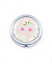 Round silver metal pill box featuring pink and white cherry blossoms on a light blue background with metallic gold details.