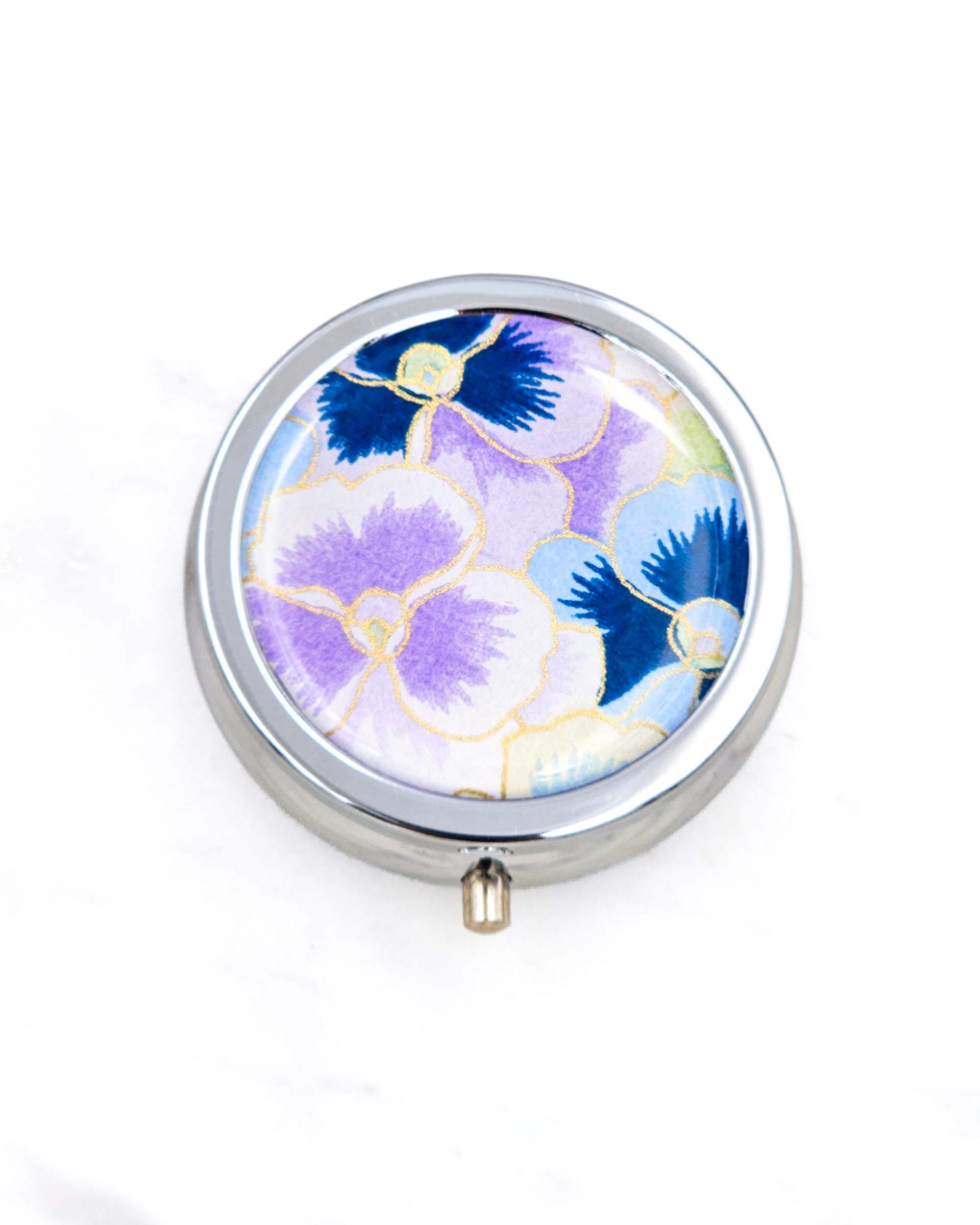 Silver metal pill box featuring purple and blue pansies background with metallic gold accents.