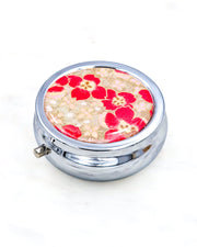 Silver metal pill box featuring red cherry blossoms on a brown background with metallic gold accents.