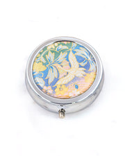 Silver metal pill box featuring a white flying crane on a green, blue , and pink pastel background with metallic gold accents.
