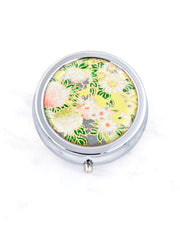 Silver metal pill box featuring assorted white flowers on a green background with metallic gold accents.