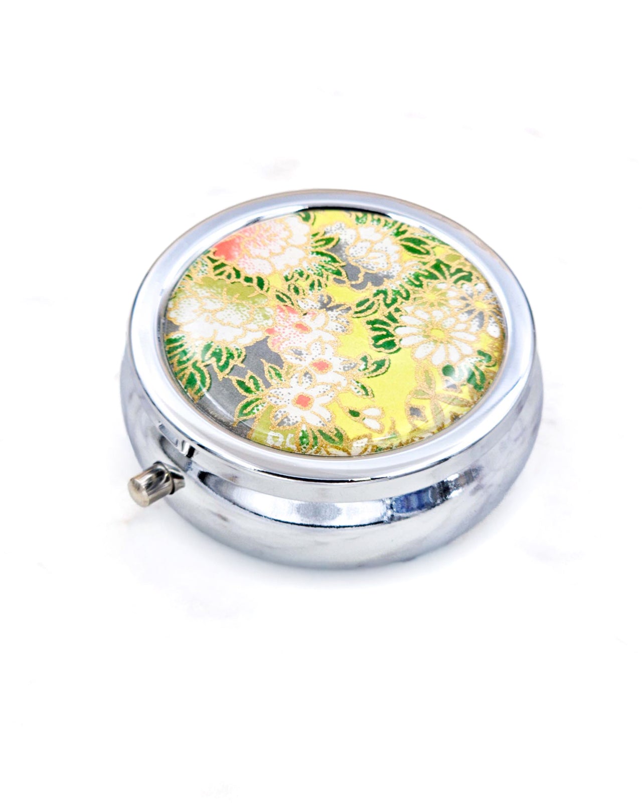 Silver metal pill box featuring assorted white flowers on a green background with metallic gold accents.