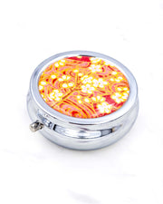 Silver metal pill box featuring white plum blossom branches on a maroon red background with metallic gold accents.