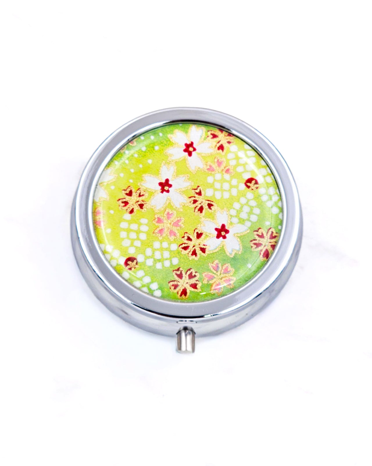 Silver metal pill box featuring white and red cherry blossoms on a green background with metallic gold accents.