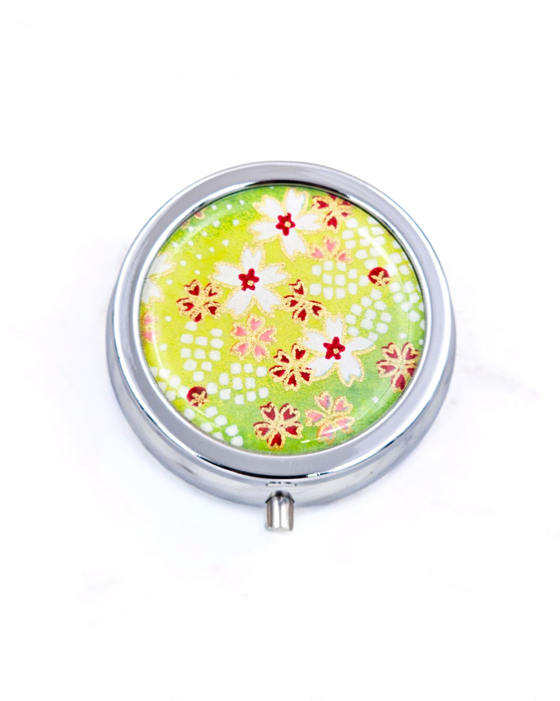 Silver metal pill box featuring white and red cherry blossoms on a green background with metallic gold accents.