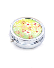 Silver metal pill box featuring white and red cherry blossoms on a green background with metallic gold accents.