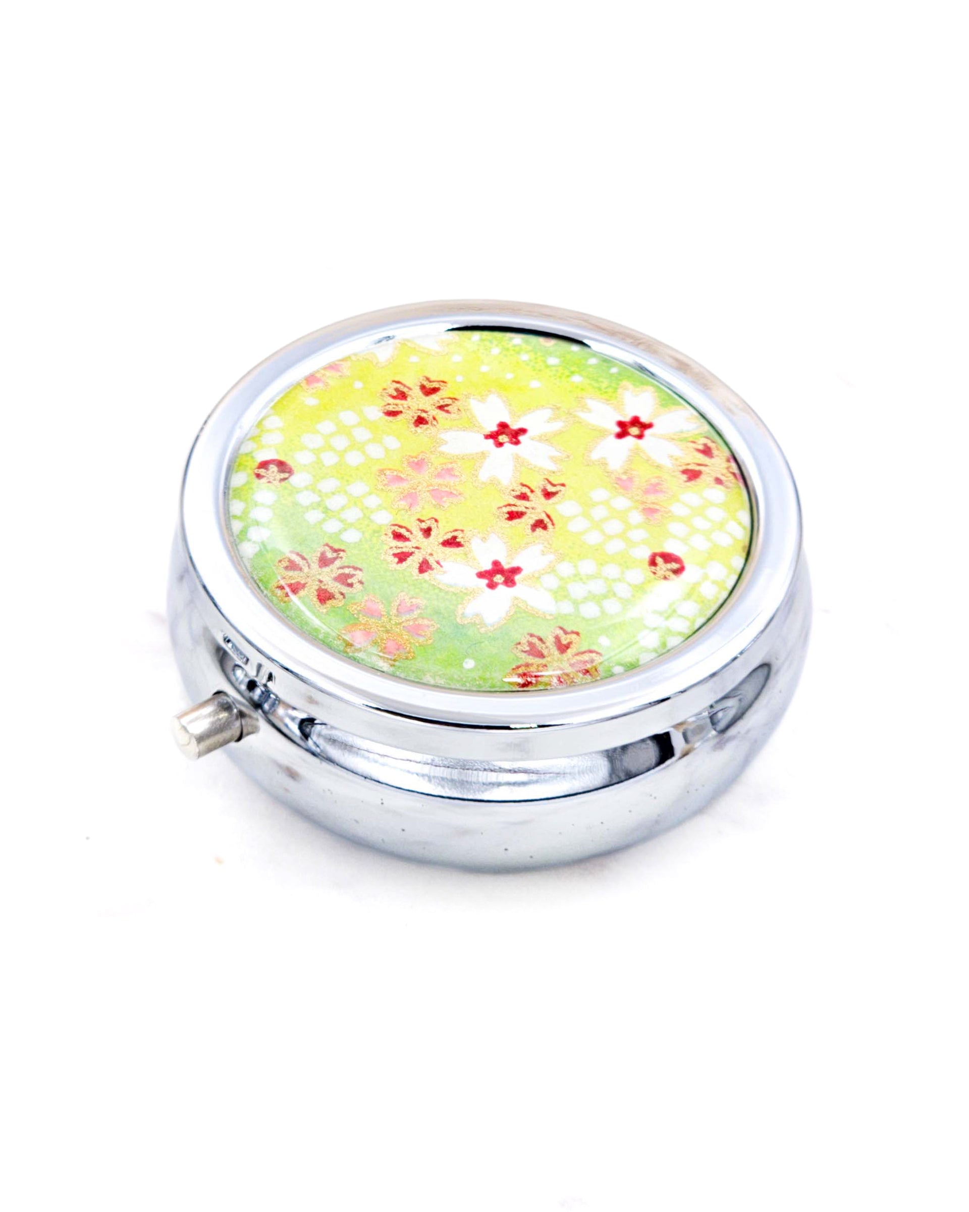 Silver metal pill box featuring white and red cherry blossoms on a green background with metallic gold accents.