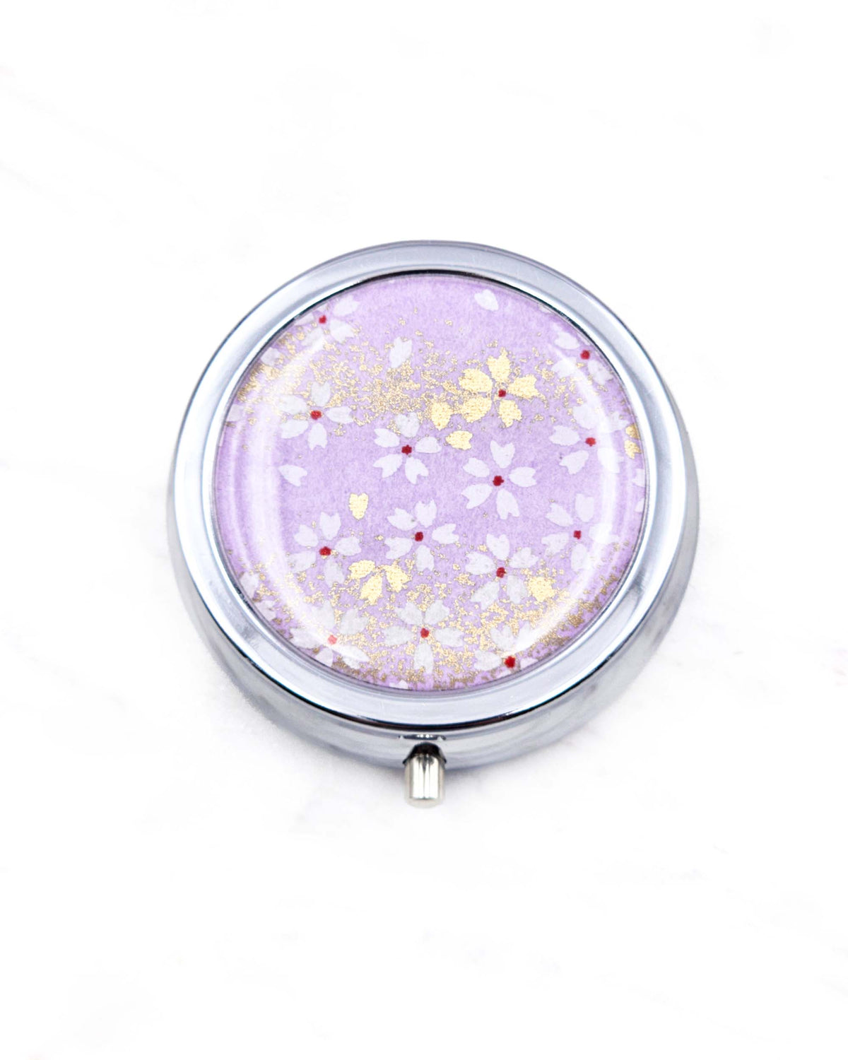 Round silver metal pill box featuring small white and gold cherry blossoms on a purple background with metallic gold details.