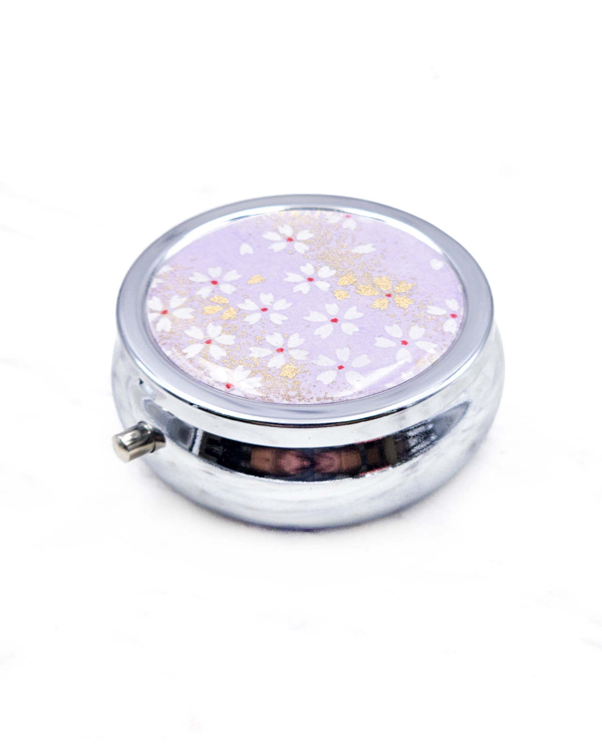 Round silver metal pill box featuring small white and gold cherry blossoms on a purple background with metallic gold details.