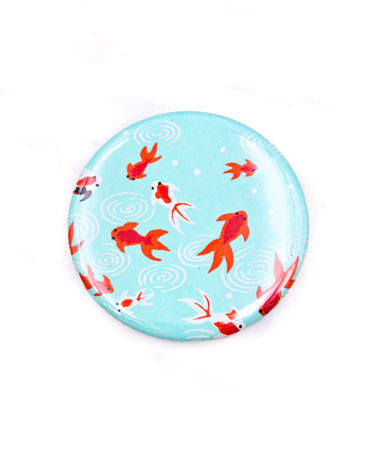 Round pocket mirror featuring red and white koi fishes on a turquoise blue background.