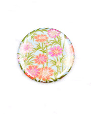 Round pocket mirror featuring pink and orange flower stalks on a light blue background with metallic gold accents.