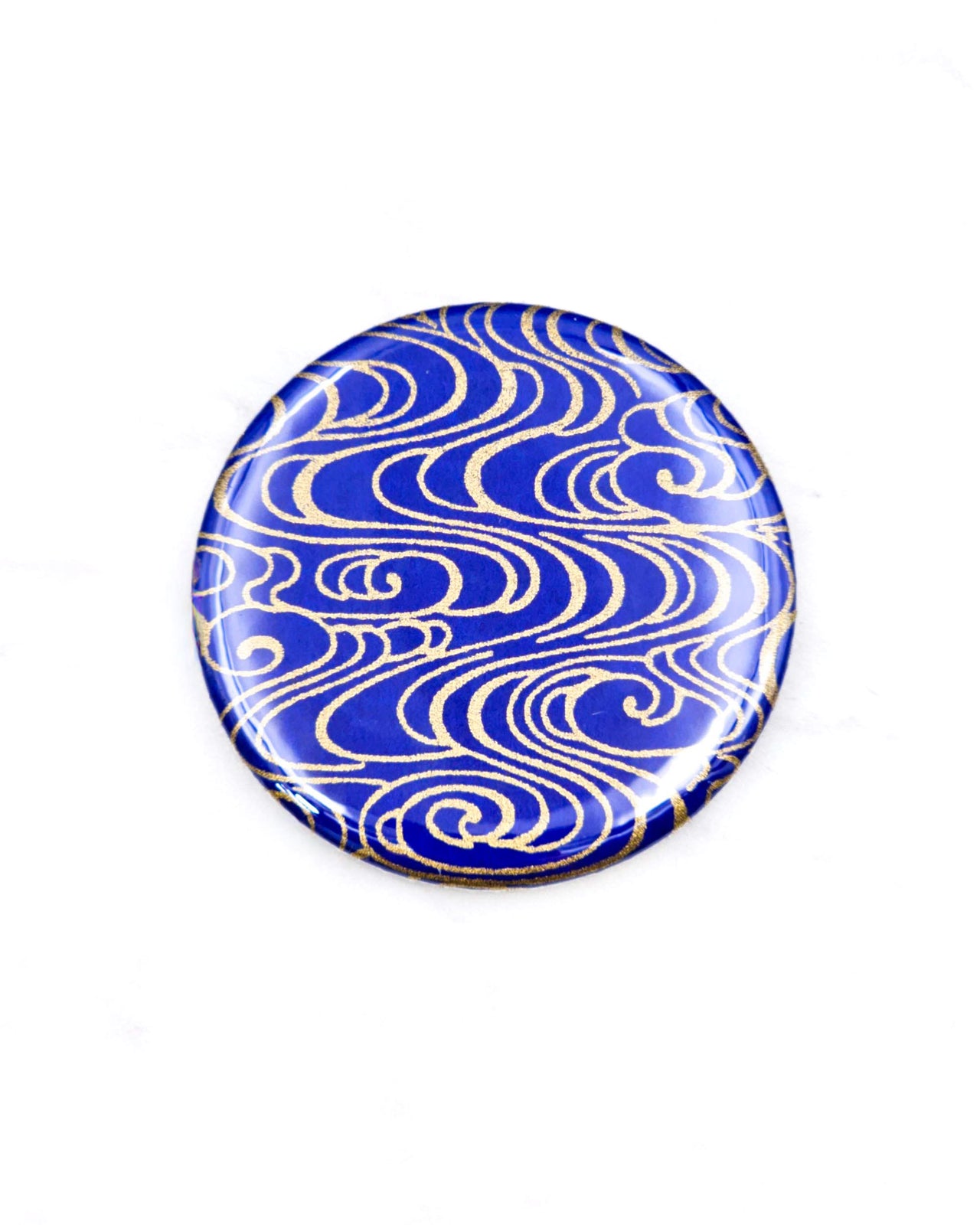 Round pocket mirror featuring metallic gold water ripples on a dark blue background.