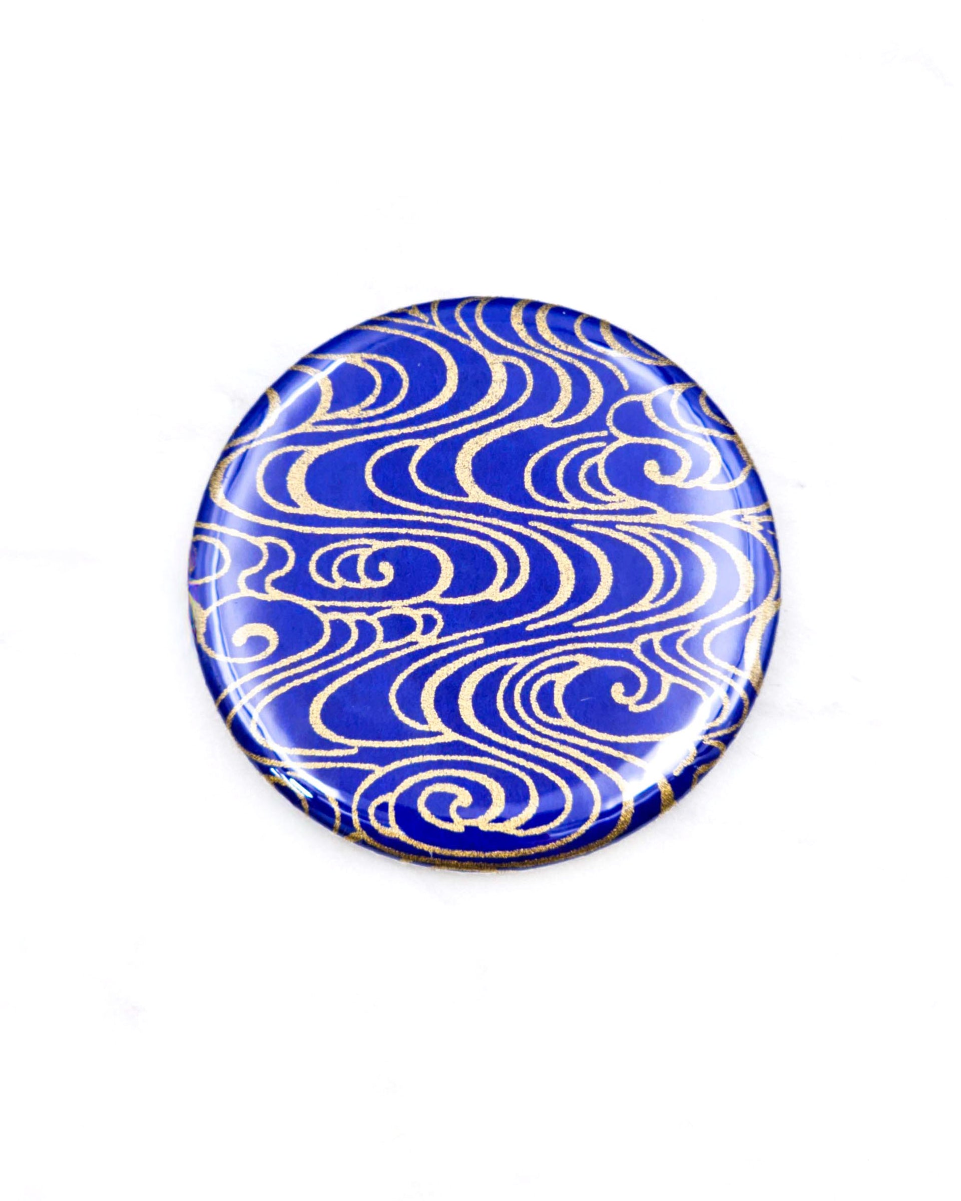 Round pocket mirror featuring metallic gold water ripples on a dark blue background.