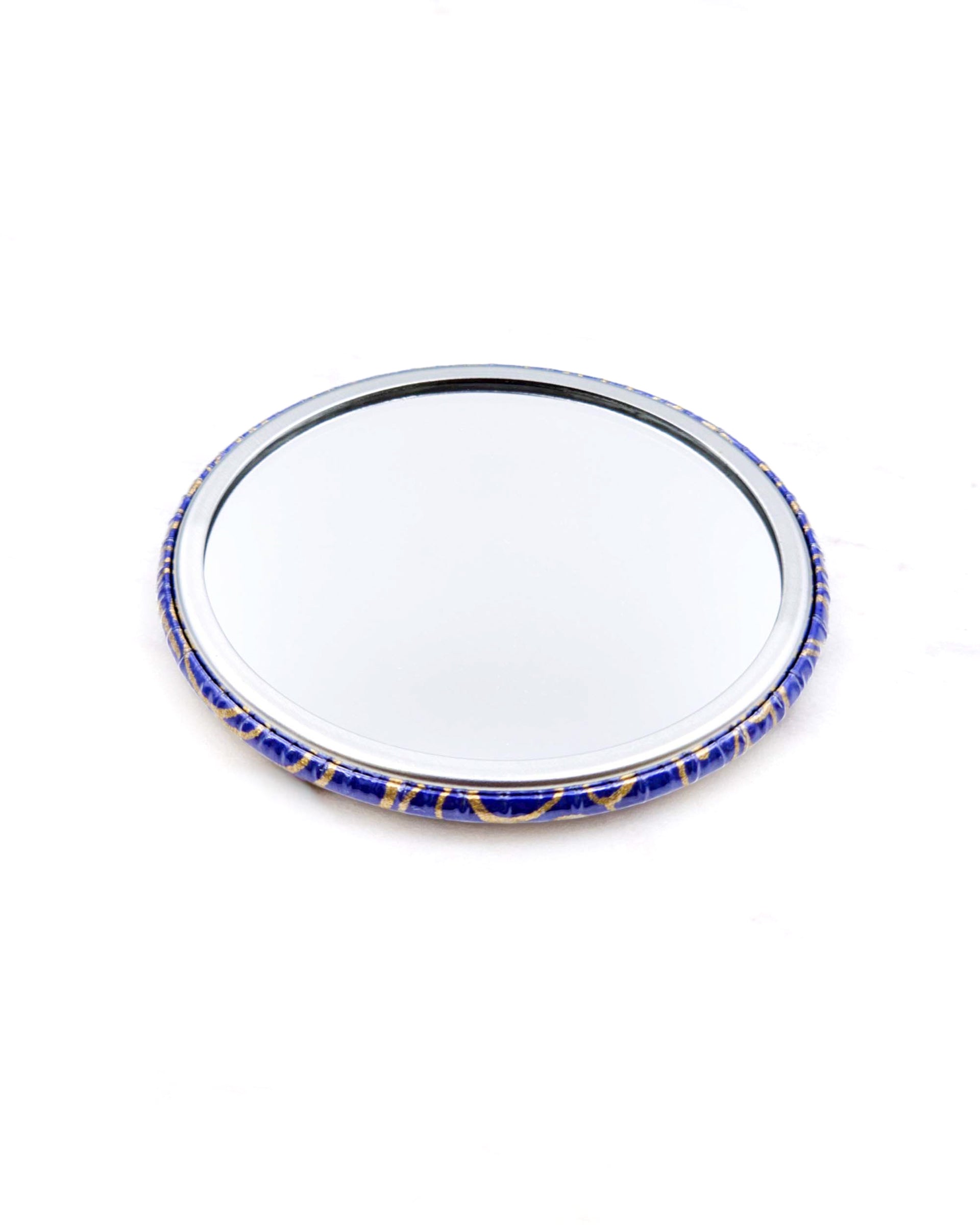 Round pocket mirror featuring metallic gold water ripples on a dark blue background.