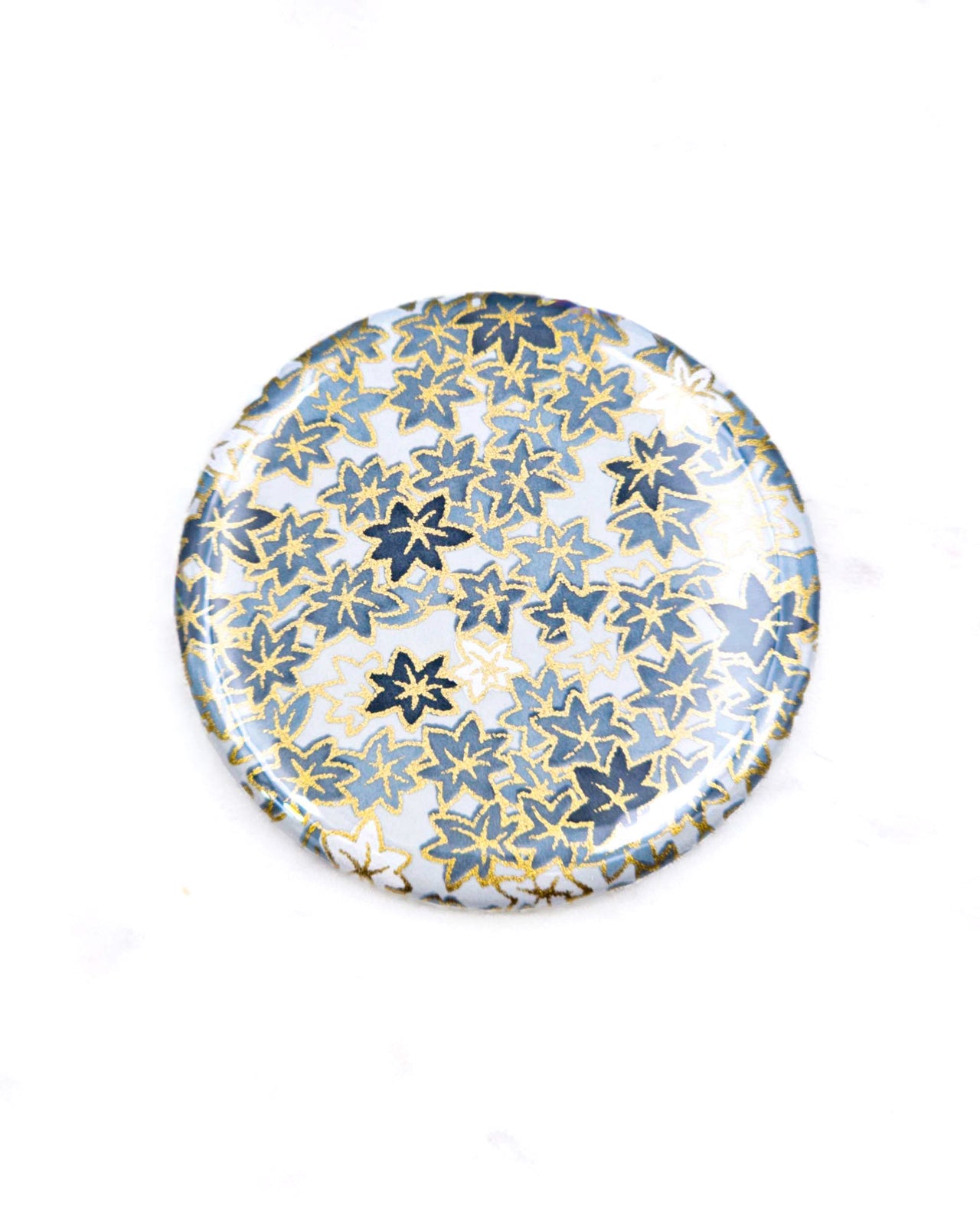 Round pocket mirror featuring gray and white maple leaves with metallic gold accents.