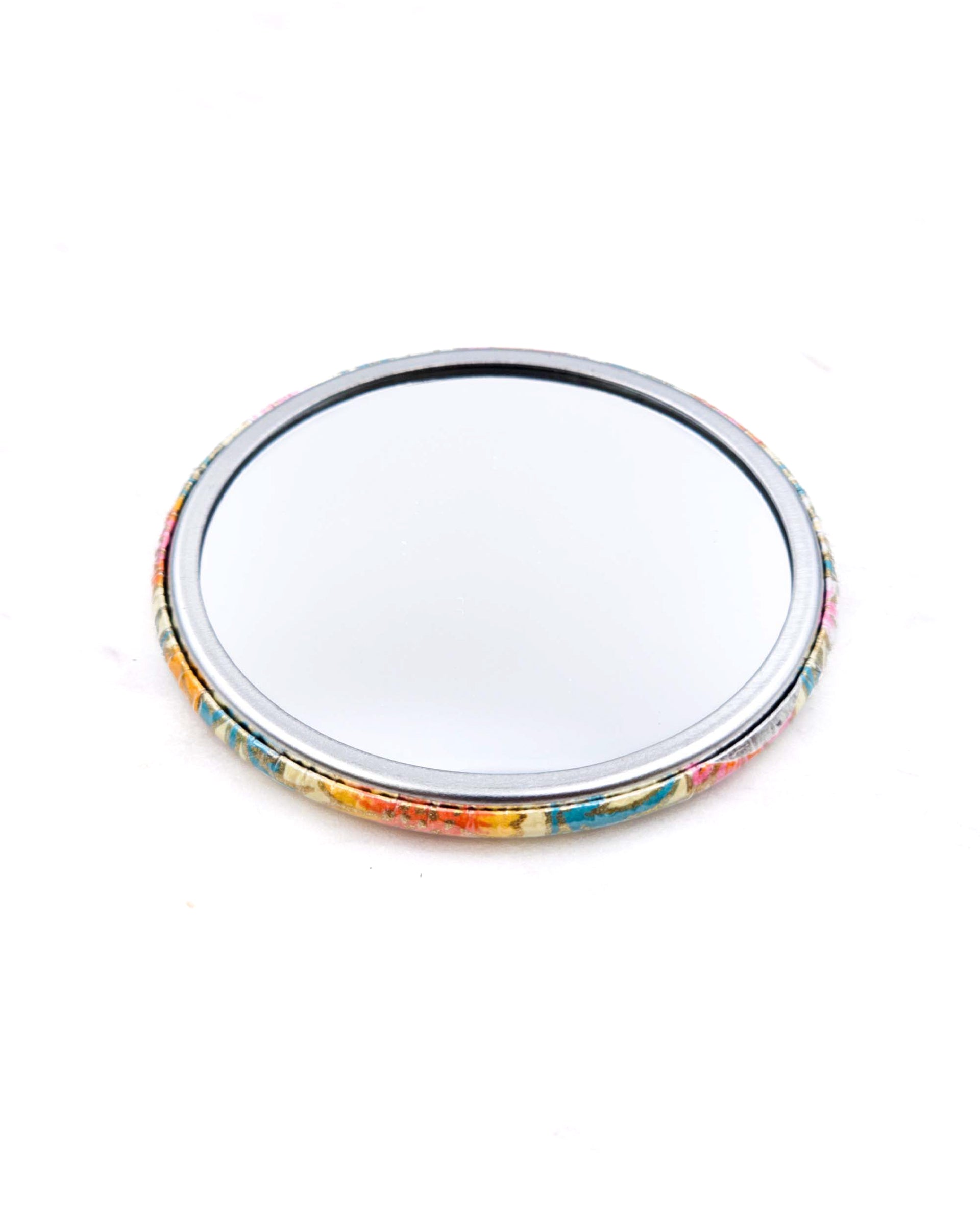 Round pocket mirror featuring orange and white flower stalks on a beige background with metallic gold accents.