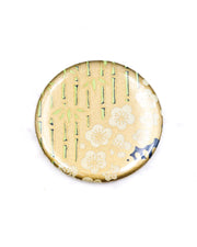 Round pocket mirror featuring cream plum blossoms and green bamboos on a metallic gold background.