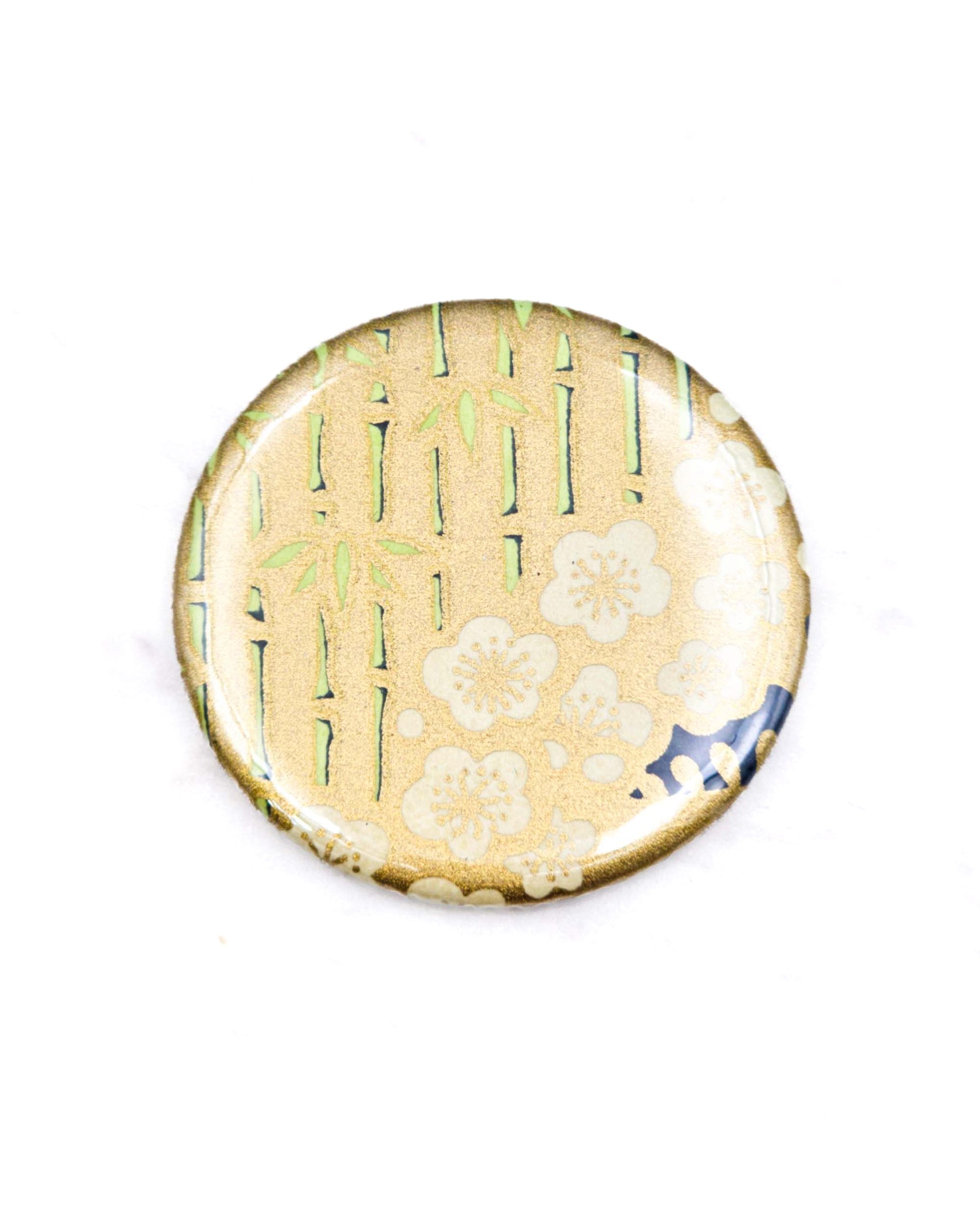 Round pocket mirror featuring cream plum blossoms and green bamboos on a metallic gold background.