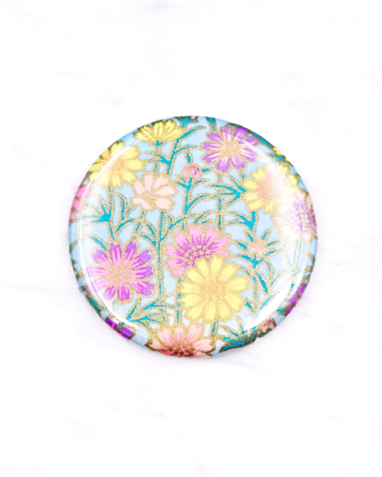 Round pocket mirror featuring yellow flower stalks on a light blue background with metallic gold accents.