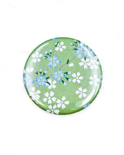 Round pocket mirror featuring small white and blue cherry blossoms on a pearlescent green background.