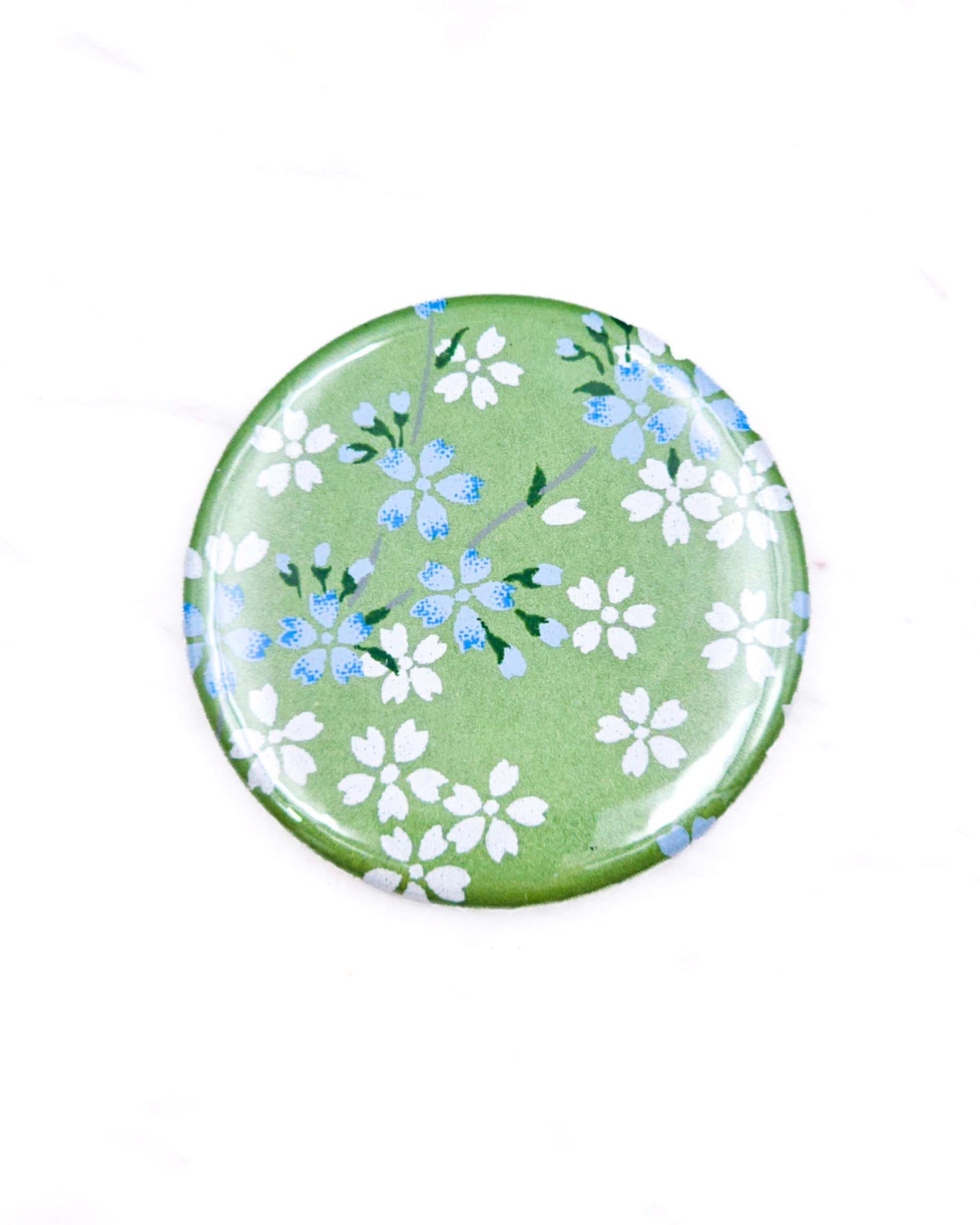 Round pocket mirror featuring small white and blue cherry blossoms on a pearlescent green background.