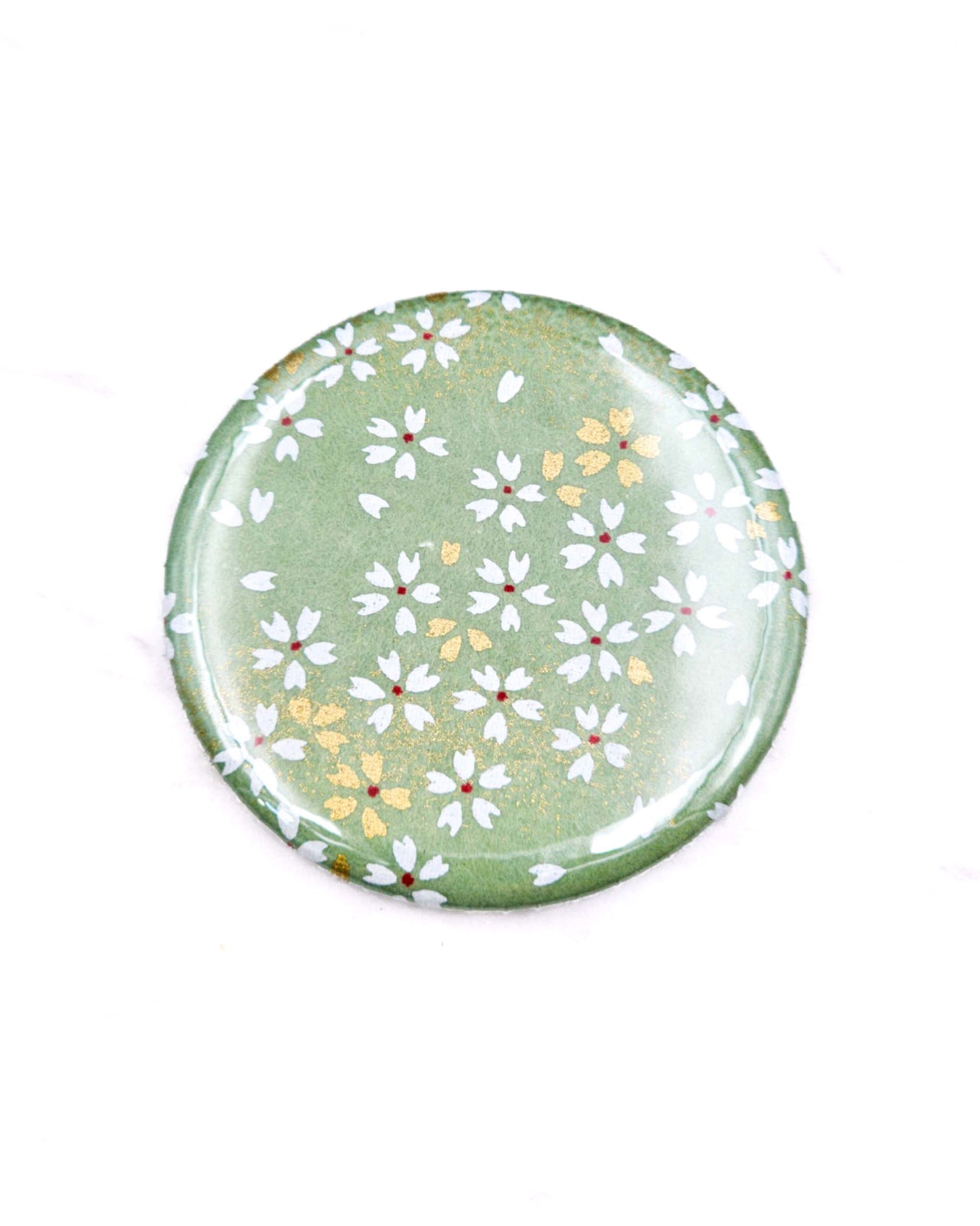 Round pocket mirror featuring small white and gold cherry blossoms on a light green background with metallic gold accents.