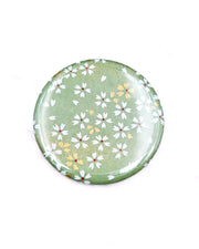 Round pocket mirror featuring small white and gold cherry blossoms on a light green background with metallic gold accents.