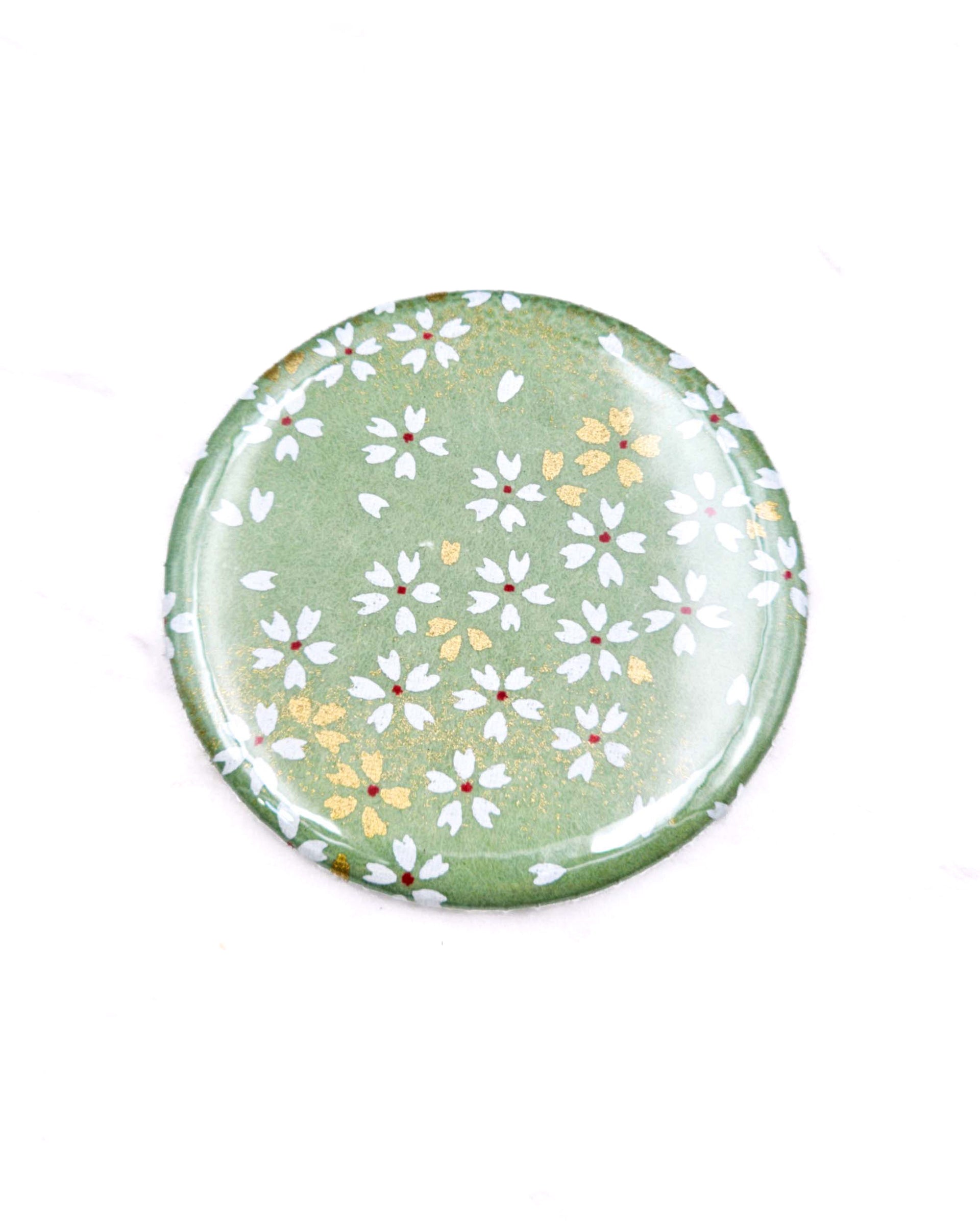 Round pocket mirror featuring small white and gold cherry blossoms on a light green background with metallic gold accents.