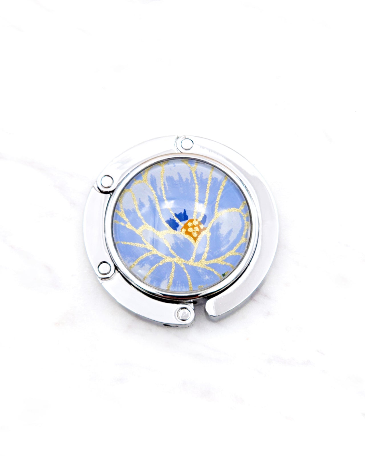Round silver metal table-top bag hanger featuring a large blue chrysanthemum flower with metallic gold details.