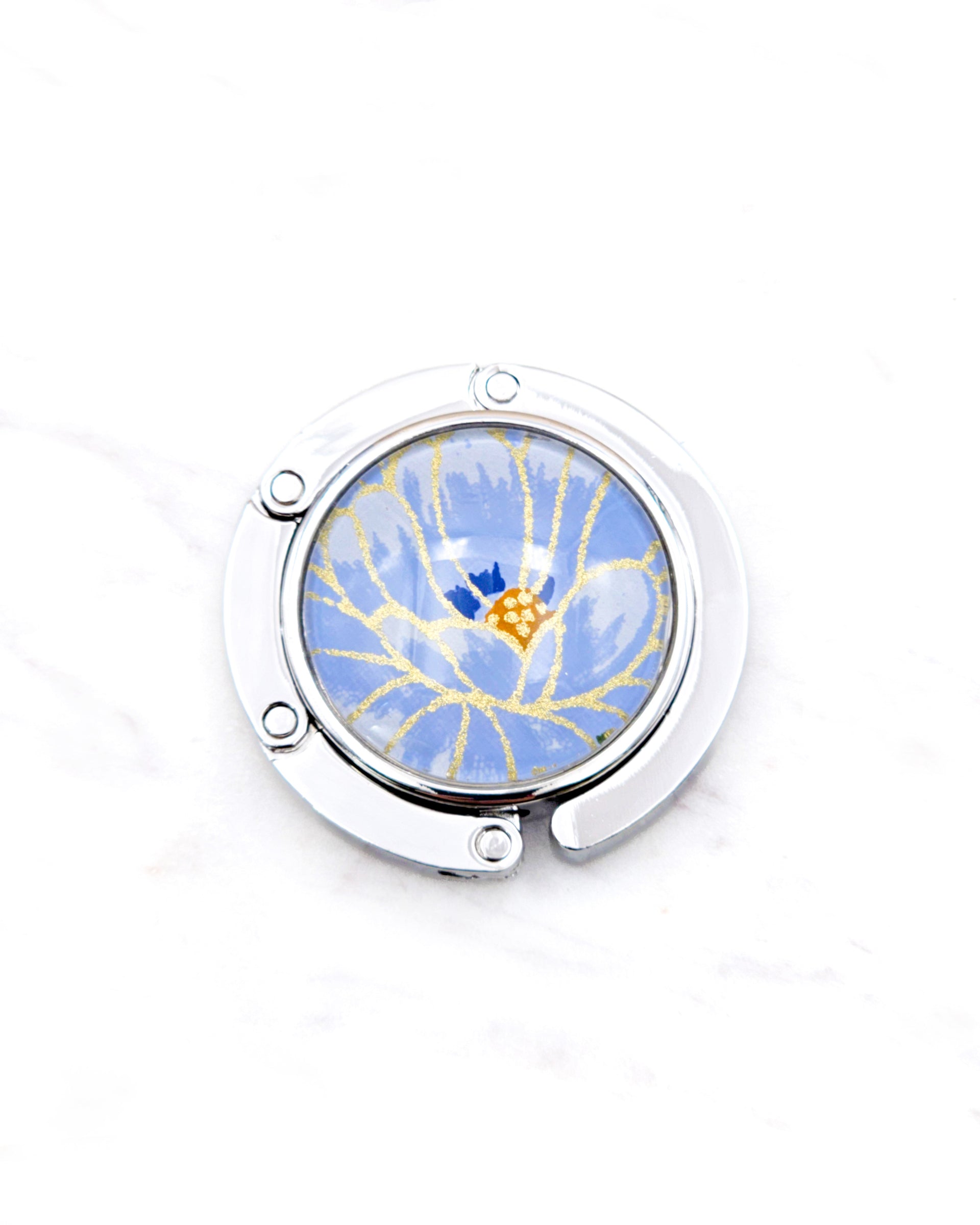 Round silver metal table-top bag hanger featuring a large blue chrysanthemum flower with metallic gold details.