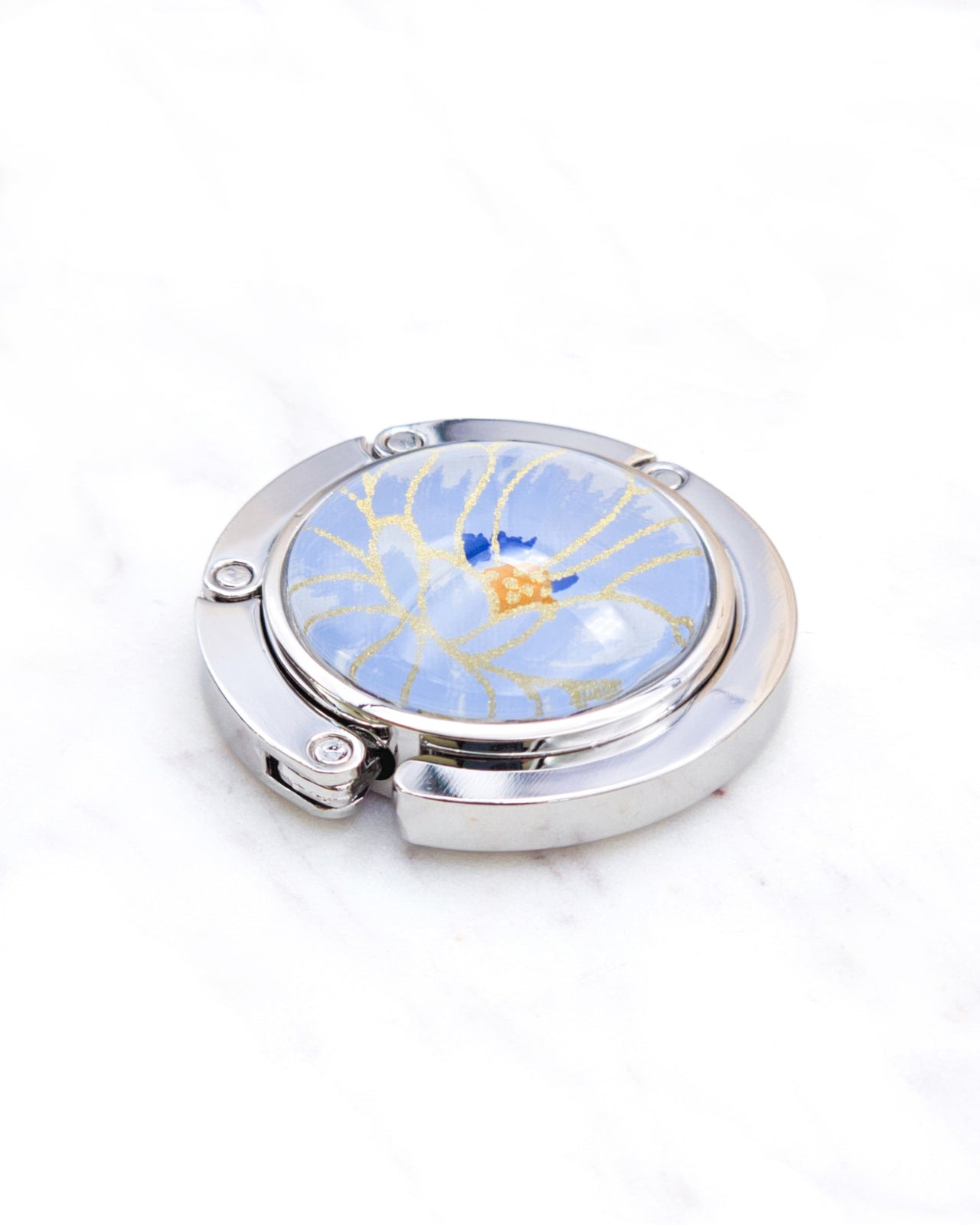 Round silver metal table-top bag hanger featuring a large blue chrysanthemum flower with metallic gold details.