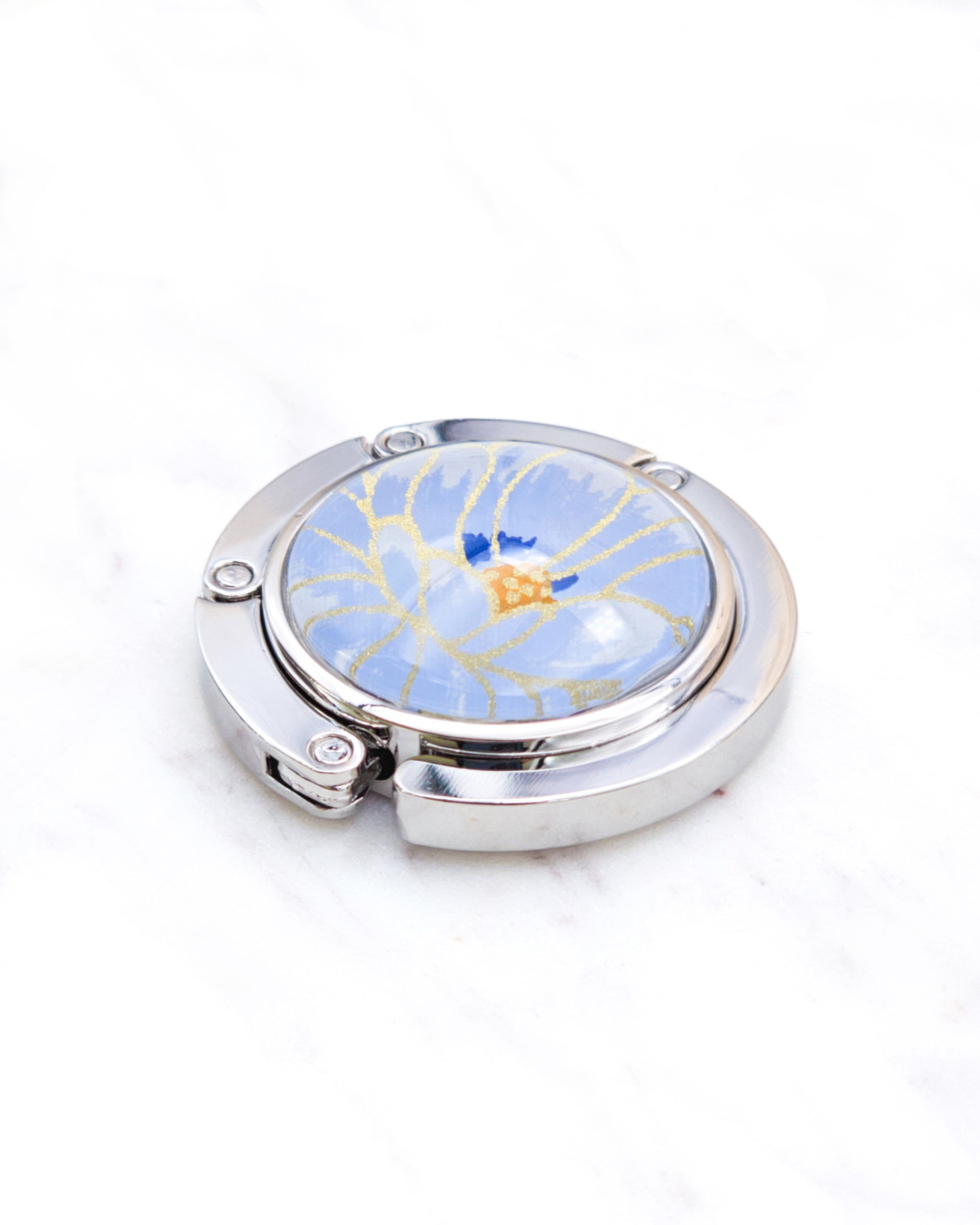 Round silver metal table-top bag hanger featuring a large blue chrysanthemum flower with metallic gold details.