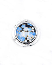 Round silver metal tabletop bag hanger featuring blue and white plum blossoms on a black background with metallic gold details.