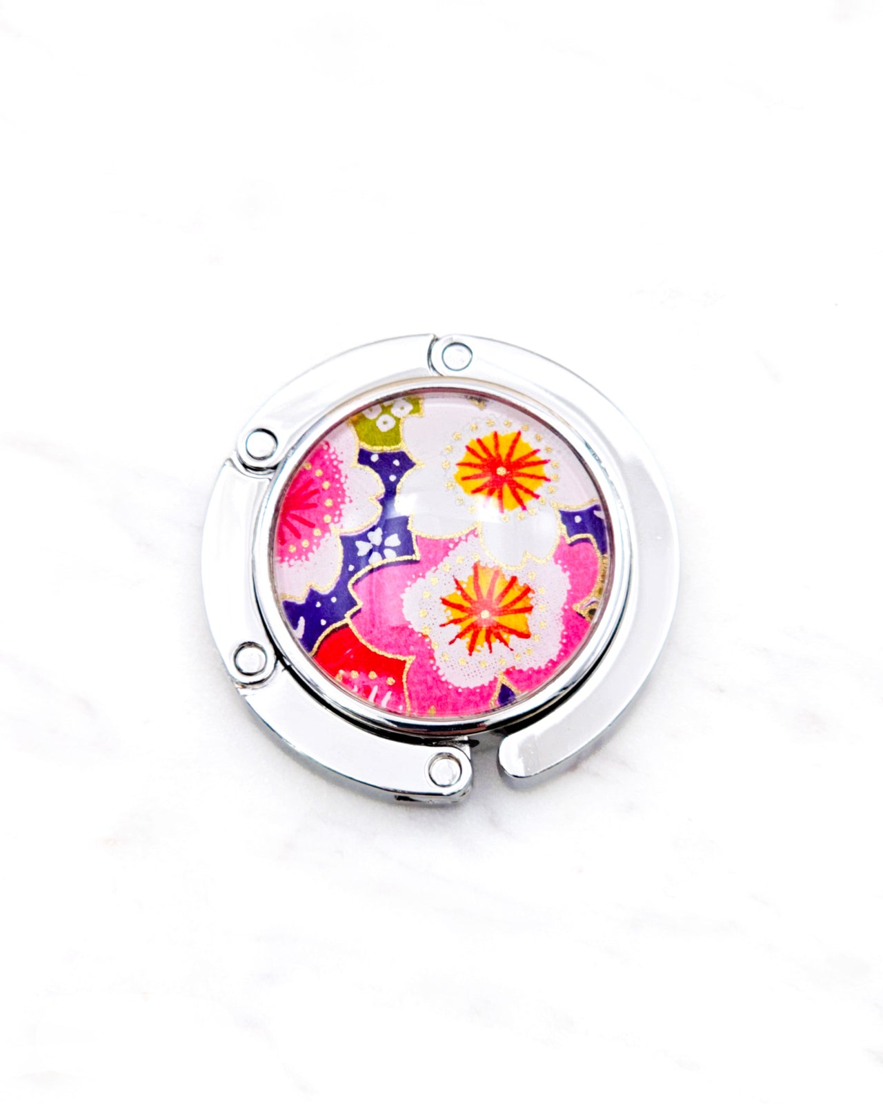 Round silver metal table-top bag hanger featuring pink and white cherry blossoms on a dark purple background with metallic gold details.