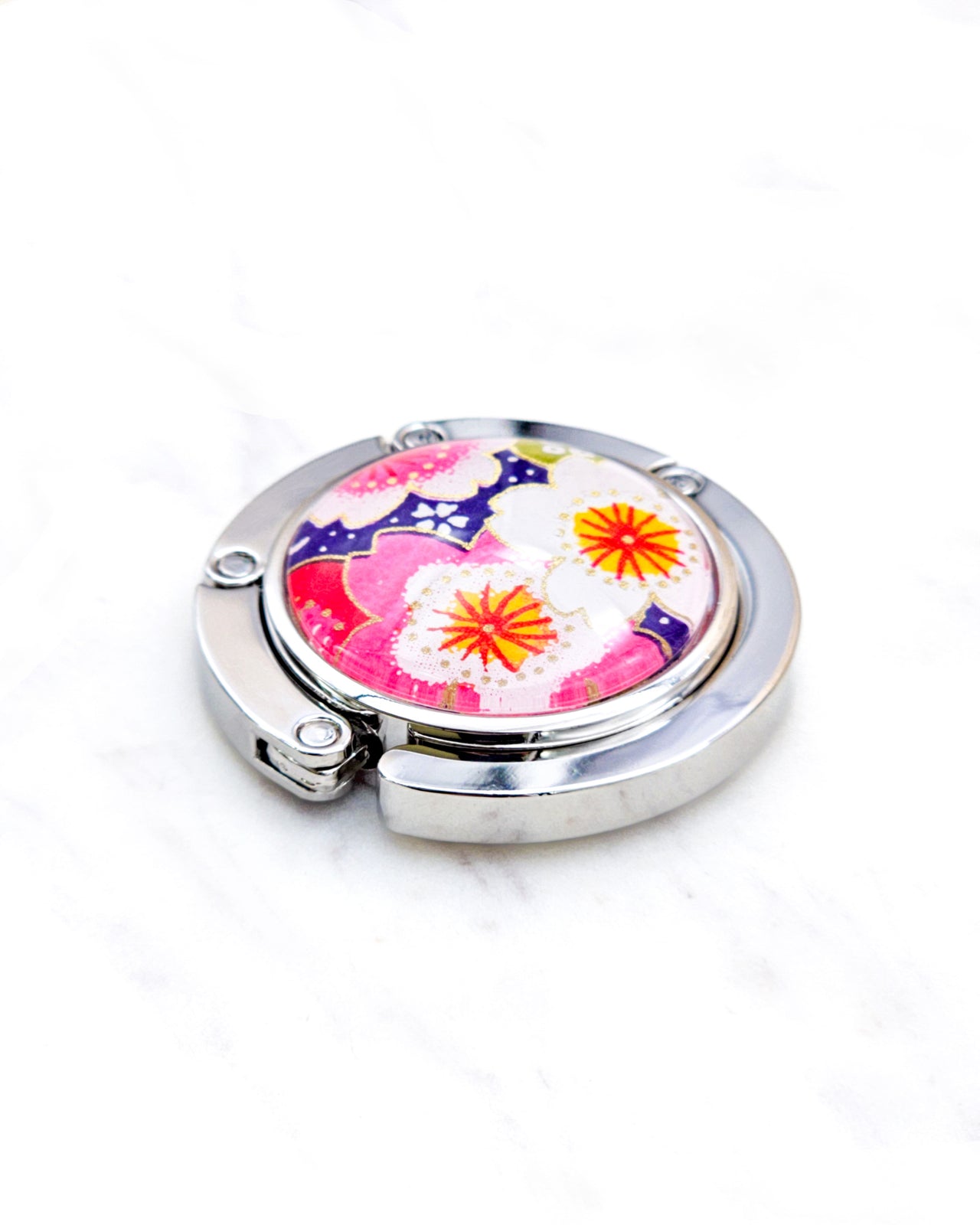 Round silver metal table-top bag hanger featuring pink and white cherry blossoms on a dark purple background with metallic gold details.