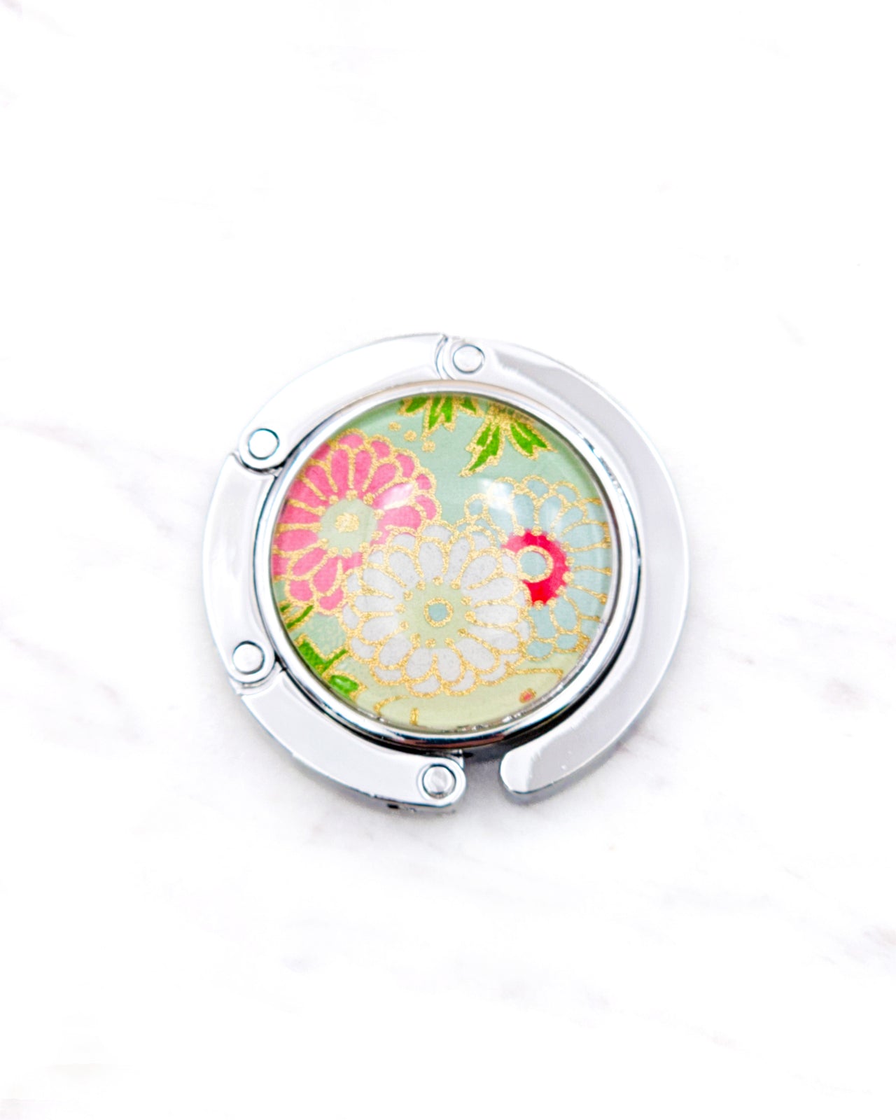 Round silver metal table-top bag hanger featuring pink, white, and green chrysanthemums on a light green background with metallic gold accents.