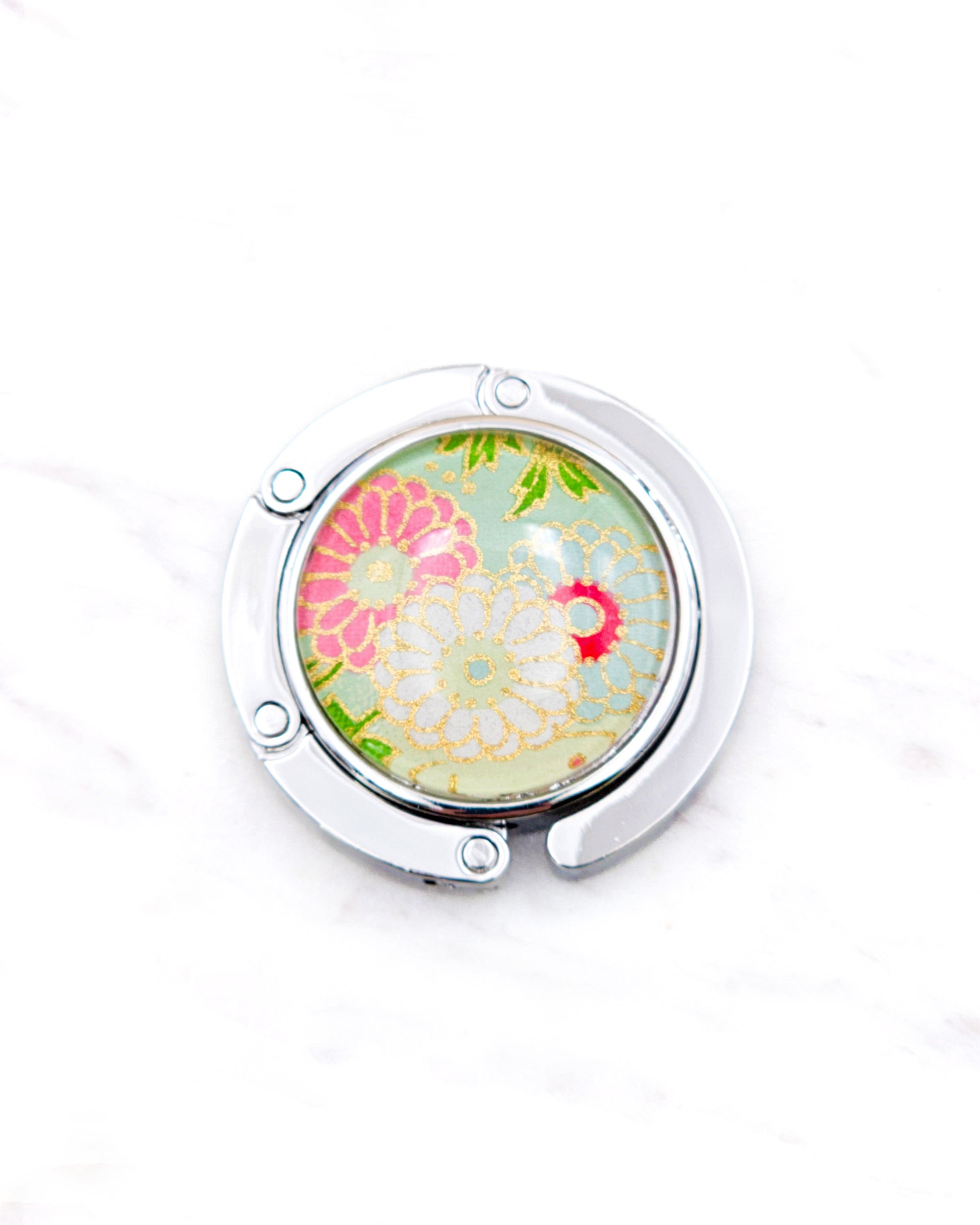 Round silver metal table-top bag hanger featuring pink, white, and green chrysanthemums on a light green background with metallic gold accents.