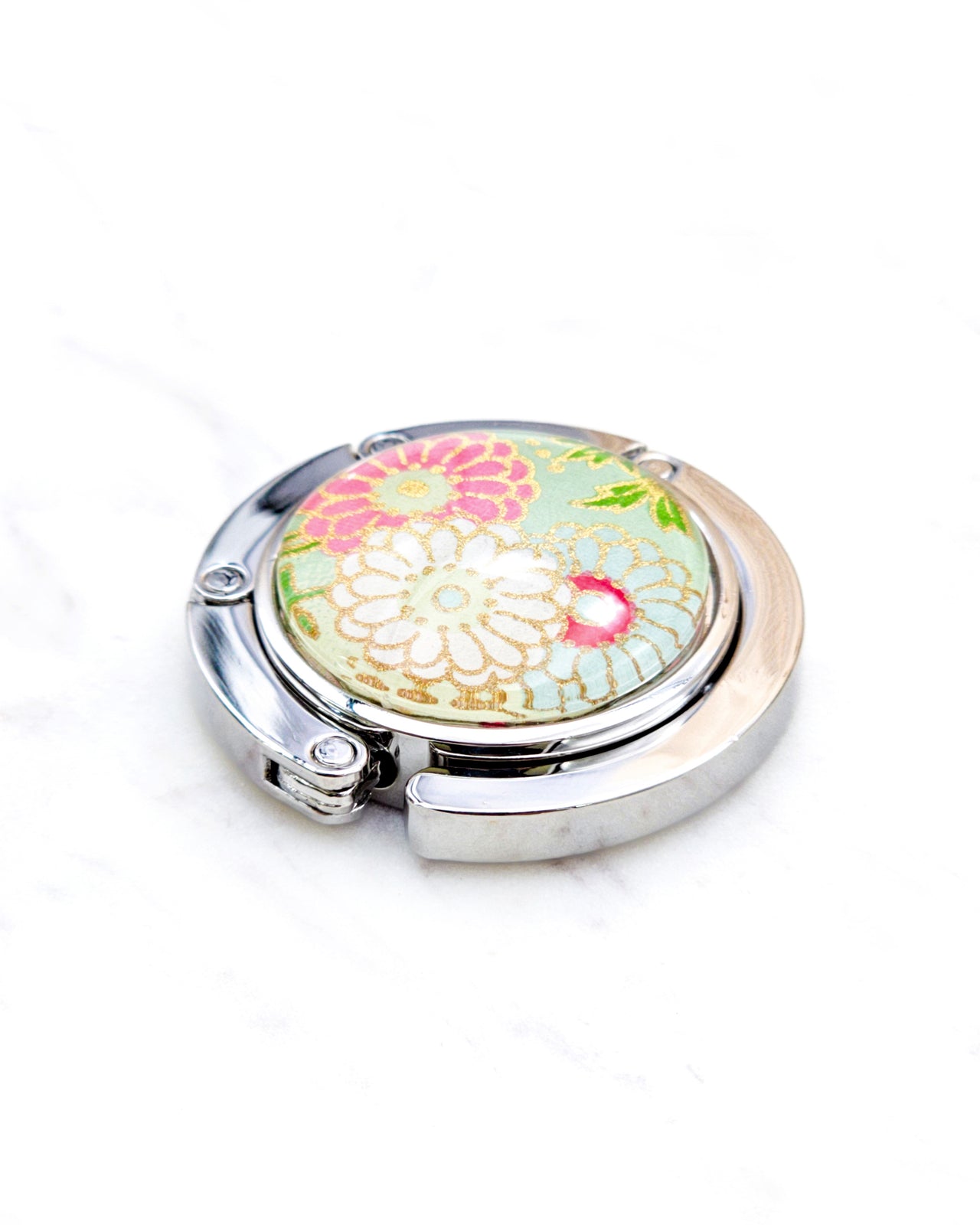 Round silver metal table-top bag hanger featuring pink, white, and green chrysanthemums on a light green background with metallic gold accents.