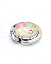 Round silver metal table-top bag hanger featuring pink, white, and green chrysanthemums on a light green background with metallic gold accents.