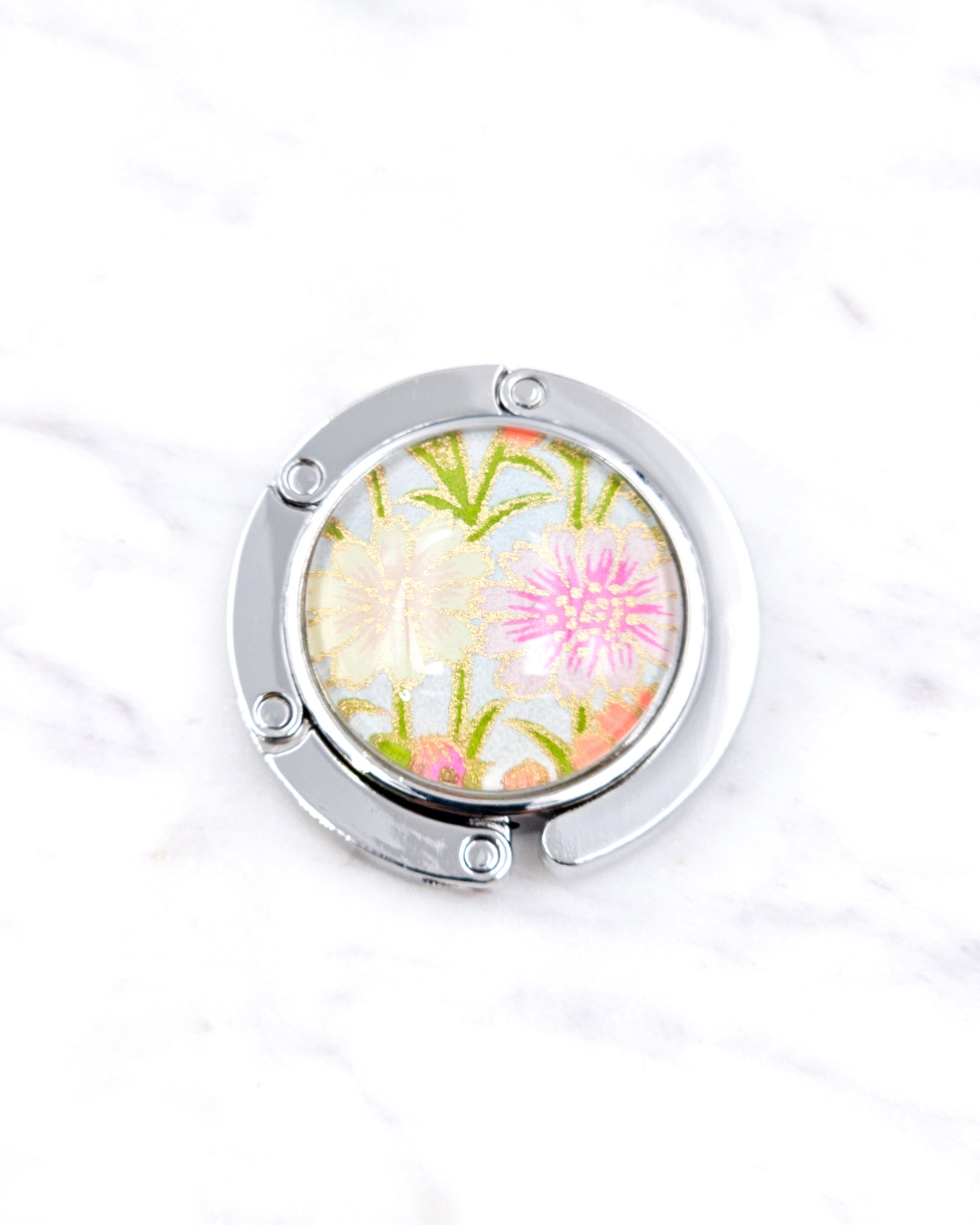 Silver metal table-top bag hanger featuring cream and pink flowers on a light blue background with metallic gold accents.