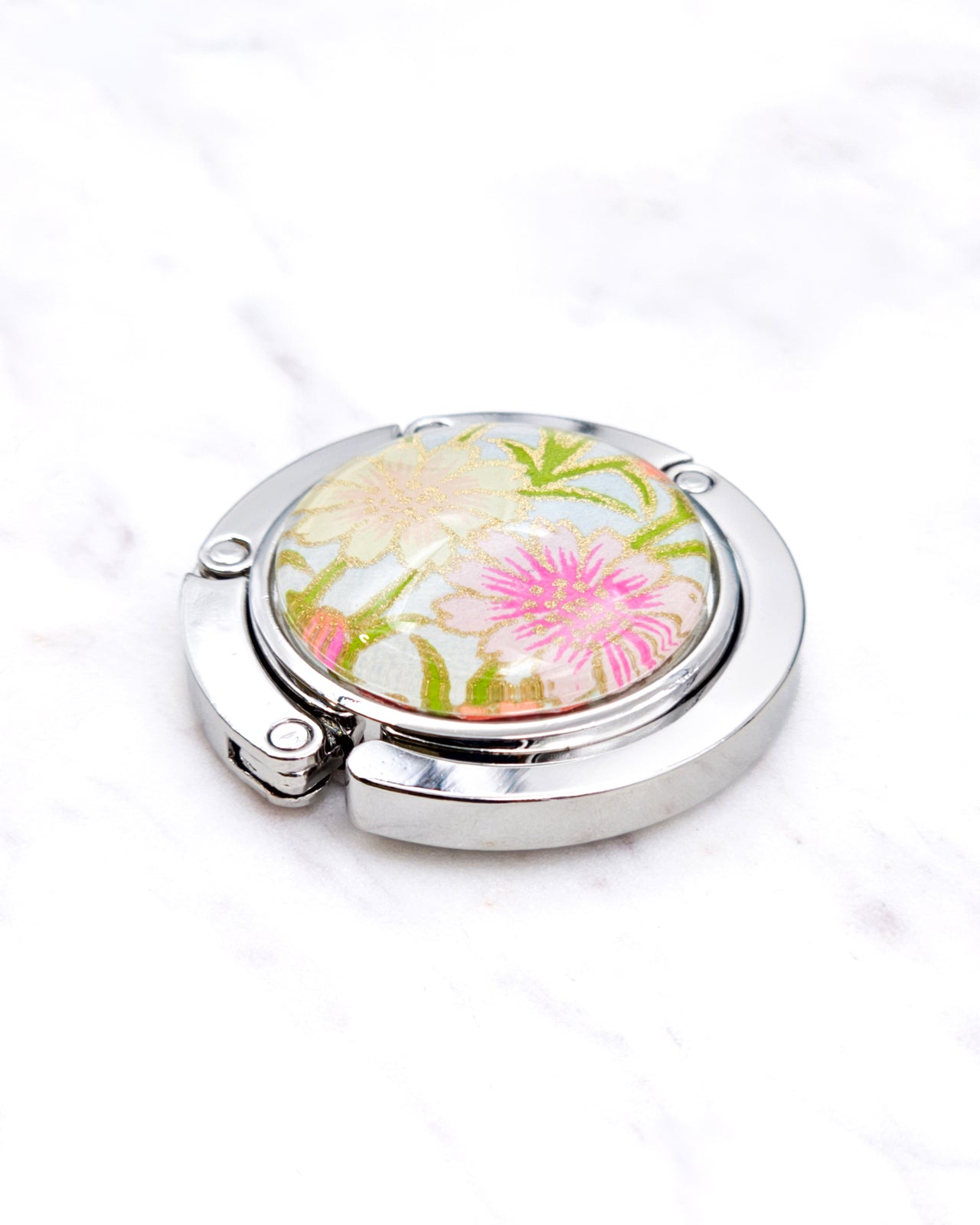 Silver metal table-top bag hanger featuring cream and pink flowers on a light blue background with metallic gold accents.