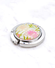 Silver metal table-top bag hanger featuring cream and pink flowers on a light blue background with metallic gold accents.